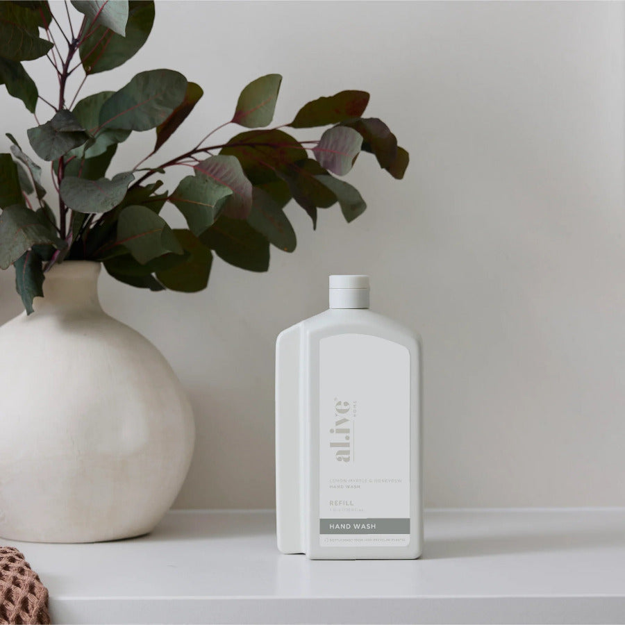 White bottle labeled 'alive' on a shelf with a vase and plant